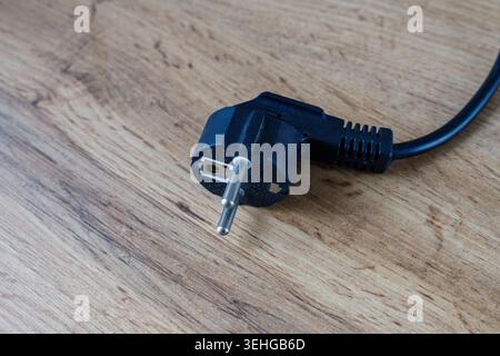 Schwarzer elektrischer Kunststoffstecker mit Metallstiften, die nicht eingesteckt auf einem Holztisch liegen. Trennen Sie das Gerätekabel, bevor Sie es in die Steckdose stecken. Konzept von Stockfoto