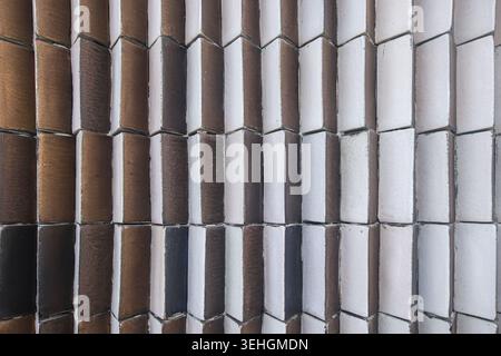 Geschwungene keramische Wandfliesen in Braun- und Grautönen bilden einen geometrischen architektonischen Fassadenhintergrund. Stockfoto