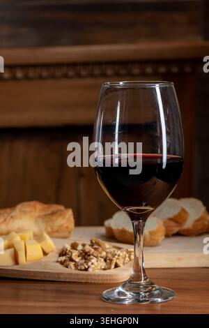 Glas Rotwein mit Brot und Käse auf rustikalem Holztisch Stockfoto