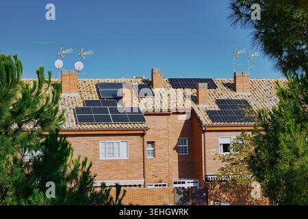 Solarpaneele auf Ziegeldächern von Wohnhäusern mit TV-Antennen unter klarem blauem Himmel. Stockfoto