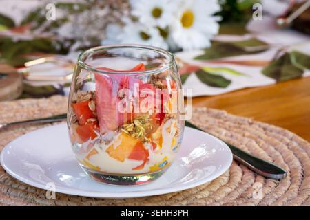 Farbenfrohes Obst-Joghurt-Parfait mit Müsli und frischer Wassermelone, serviert in einem Glas auf einem stilvollen Frühstückstisch. Stockfoto