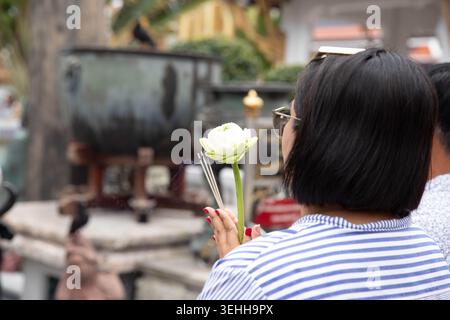 Thailändische Frau, die Lotus und Weihrauch respektiert, Touristen, die spirituelle Atmosphäre im Tempel erleben, aus nächster Nähe Stockfoto
