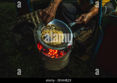 Nahaufnahme eines Straßenkühlers, der mit einem Löffel Ei und klebrigen Reis in einer Pfanne über einem glühenden Holzkohleofen mixte, um kerak Telor zu kochen. Stockfoto