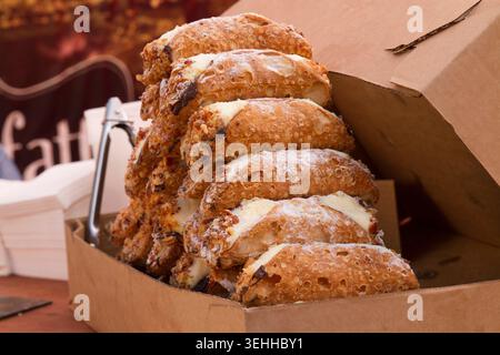 Ein hoher Stapel frischer italienischer Cannoli-Gebäckstücke, gefüllt mit Sahne und bestäubt mit Zucker in einem Karton. Stockfoto