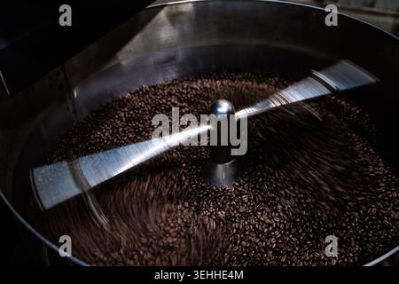 Handgefertigte Kaffeebohnen, die in einer Kühlmaschine aus Edelstahl zirkulieren, um eine gleichmäßige Kühlung und Qualität während des professionellen Röstprozesses zu gewährleisten. Stockfoto