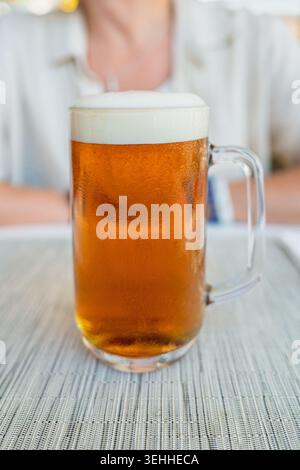 Erfrischende Tasse goldenes Bier mit Schaumstoffkopf, kalt auf einem Tisch im Freien serviert, isoliert Stockfoto