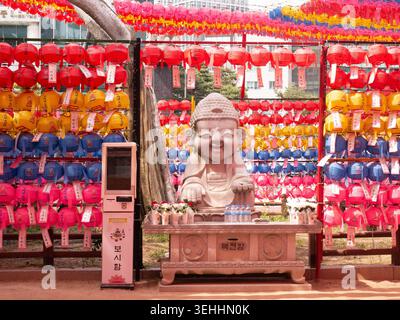 Lächelnde kleine Buddha-Statue aus Stein zwischen farbenfrohen Laternen im Jogyesa-Tempel, Seoul. Stockfoto