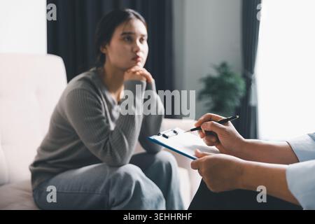 Junge Frau, die während der psychischen Gesundheitsberatung zuhört, während die Therapeutin Notizen schreibt, die Psychotherapie, Reflexion, Angstunterstützung, t repräsentieren Stockfoto