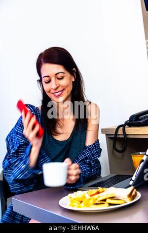 Frau, die während der morgendlichen Frühstücksroutine aus der Ferne arbeitet Stockfoto