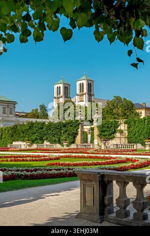 Wunderschöner Blick auf die formellen Blumenbeete im Mirabellgarten mit den Türmen der Andreas-Kirche im Hintergrund an einem hellen sonnigen Tag in Salzburg Stockfoto