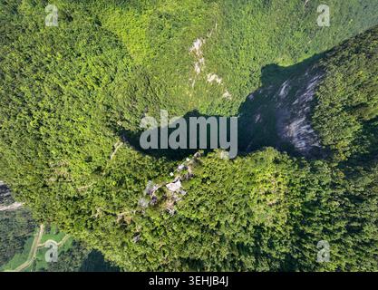 Drohnenansicht aus der Vogelperspektive eines Riesenkarstswinklochs, umgeben von dichtem Wald in der Präfektur Qiannan, Guizhou, China Stockfoto