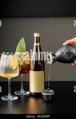 Mann, der Drink in Glas gießt, neben Flasche und Cocktails. Studio leichte, professionelle Komposition. Leerzeichen für Text Stockfoto