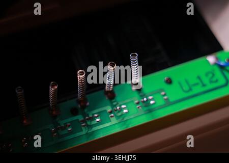 Nahaufnahme der grünen Leiterplatte mit nach oben ragenden metallischen Federkomponenten, die ein Gefühl technischer Präzision und komplexer Elektronik erzeugen Stockfoto
