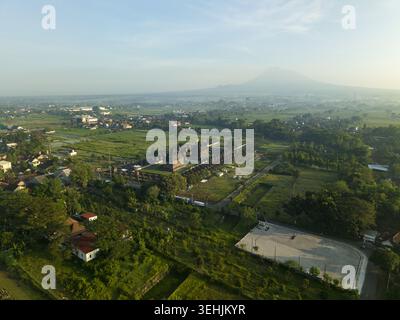 Aus der Vogelperspektive des Tempelkomplexes Plaosan Lor umgeben von grünen Feldern mit dem Berg Merapi im Hintergrund Kecamatan Prambanan, Jawa Tengah, Indonesien. Stockfoto