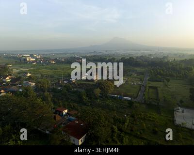 Blick aus der Vogelperspektive auf den Plaosan Lor Tempelkomplex, umgeben von üppigen grünen Feldern und Wohnhäusern mit Mount Merapi im Hintergrund Kecamatan Pramban Stockfoto