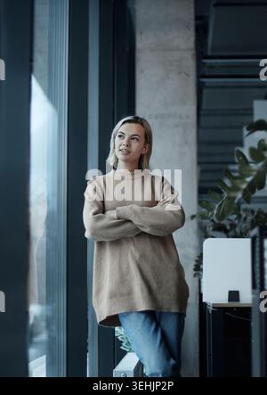Eine Frau in einem braunen Pullover steht vor einem Fenster Stockfoto