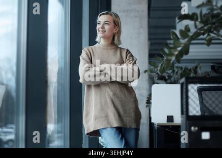 Eine Frau steht mit überkreuzten Armen vor einem Fenster Stockfoto