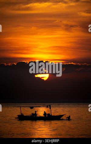 Traditionelles Fischerboot in Bali, Indonesien, vor einem dramatischen Sonnenuntergang über dem Meer. Stockfoto