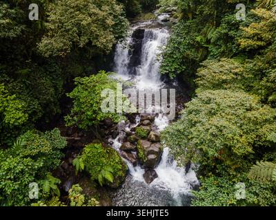 Aus der Vogelperspektive des Ambyar Wasserfalls, der durch dichten tropischen Dschungel und üppiges grünes Laub über dunklen vulkanischen Felsen in Purwokerto, Zentral-Java, I, fällt Stockfoto