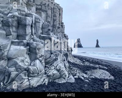 Basaltklippen und vulkanischer schwarzer Sandstrand in Reynisfjara, Island, mit den Reynisdrangar-Meeressteinen, die im Nordatlantik sichtbar sind. Stockfoto