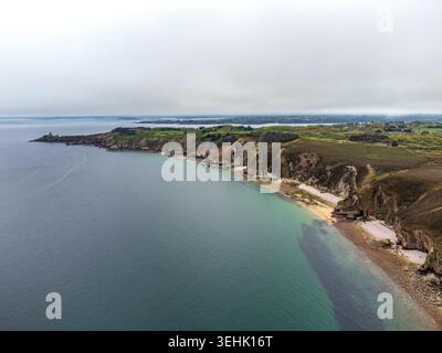 Ein weites Hochwinkelpanorama auf die bretonische Küste, wo das smaragdgrüne Meer gegen zerklüftete Klippen und einsame Buchten schlägt. In der Entfernung die Silhouette von for Stockfoto