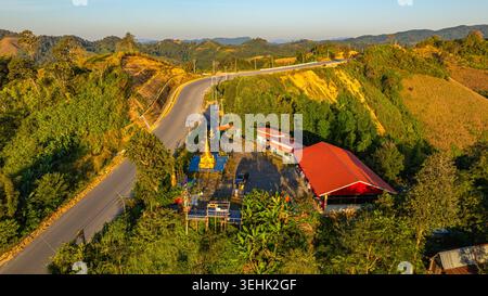 Ein atemberaubender Blick auf den Sonnenaufgang über dem Wat Ban SOP Puen in der Provinz Nan, der eine gewundene Bergstraße durch das üppige grüne Hochland zeigt. Stockfoto