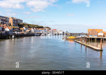 hafenszene in Whitby, North Yorkshire, zeigt Boote, die neben hölzernen Piers liegen, und ruhiges reflektierendes Wasser. Traditionelle Häuser und Geschäfte Stockfoto