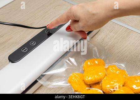 Eine Hausfrau benutzt ein Vakuumsiegel für Lebensmittel in der Küche. Verpackung von Produkten für die Langzeitlagerung. Ein Finger drückt eine Taste an einem Vakuumsiegelgerät. v Stockfoto