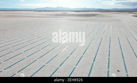 Aus der Vogelperspektive der Salinas Grandes Salinen mit türkisfarbenen Wasserkanälen unter hellem Himmel mit weit entfernten Bergen in Tumbaya, Jujuy, Argentinien. Stockfoto