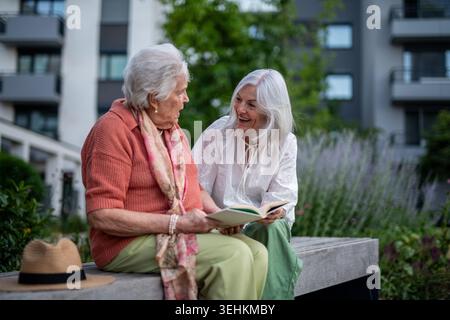 Ältere Mutter sitzt auf der Bank mit erwachsener Tochter und liest zusammen. Stockfoto
