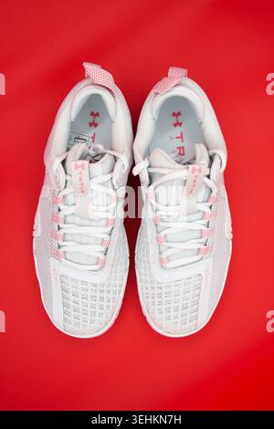 Ein Paar hellgraue Under Armour TriBase Reign 6 Trainingsschuhe mit pinkfarbenen Details auf einem leuchtend roten Hintergrund Stockfoto