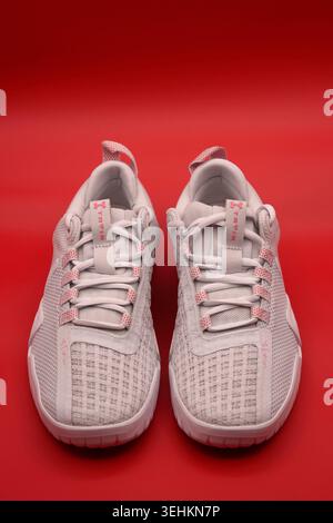 Ein Paar hellgraue Under Armour Tribase Reign 6 Trainingsschuhe mit pinkfarbenen Details auf einem leuchtend roten Hintergrund Stockfoto