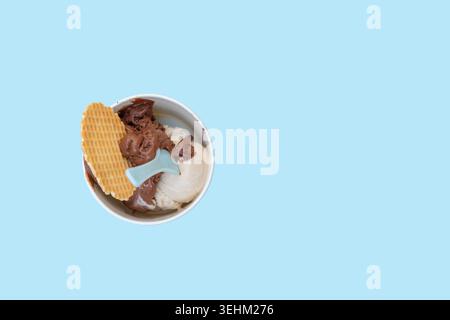Eine Tasse enthält zwei verschiedene Eissorten, Schokolade und Vanille, serviert mit einem Waffelkeks. Die Szene ist hell mit einem hellblauen Hintergrund, typisch für Stockfoto