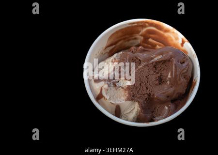 Eine Tasse mit Schokolade und Vanilleeis steht auf schwarzem Hintergrund. Schüsseln Schokoladensoße mischen sich mit dem Eis und zeigen reichhaltige Aromen. Stockfoto