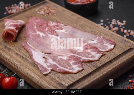Speisen, leckere Scheiben geräucherter Marmelade oder Schinken mit Salz, Gewürzen und Kräutern auf dunklem Betonhintergrund Stockfoto