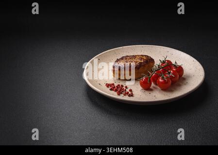 Essen, köstliches frisch gebratenes vegetarisches Sojabohnenschnitzel mit Salz, Gewürzen und Kräutern mit Gemüse auf einer Keramikplatte auf dunklem Betonhintergrund Stockfoto