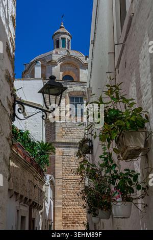 Eine schmale Gasse in Locorotondo mit Blick auf die Kuppel und den Glockenturm der Kirche San Giorgio Martyre. Locorotondo, Bari, Apulien, Italien Stockfoto