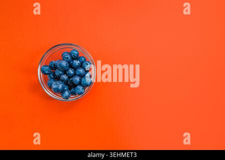 Frische Heidelbeeren in der Glasschale auf orangem Hintergrund mit negativem Raum Stockfoto