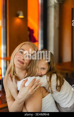 Mutter und Tochter teilen einen zärtlichen Moment in einem gemütlichen Café. Die Szene fängt das Wesen der Mutterschaft, familiäre Bindungen und die einfachen Freuden des Kindes ein Stockfoto