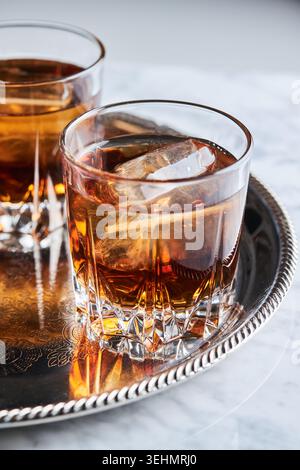 Nahaufnahme von Bourbon-Whisky, serviert auf Eis in einem geschliffenen Kristallbecher auf einem silbernen Tablett, warme Bernsteintöne und Reflexionen, elegante Bar-Stimmung, Kopierraum an Stockfoto