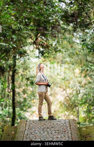 Eine Reisende mit Kamera steht auf einem Steinweg im üppigen Wald des San Agustin Archaeological Park in Kolumbien und erkundet das antike religiöse Monume Stockfoto