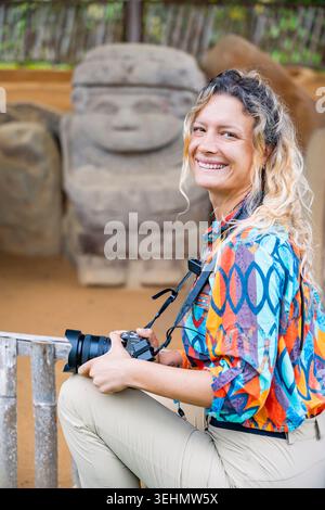 Lächelnde Reisende mit Kamera im Archäologischen Park San Agustin, Kolumbien, posiert vor antiken religiösen Steindenkmälern, die zum UNESCO-Weltkulturerbe gehören Stockfoto