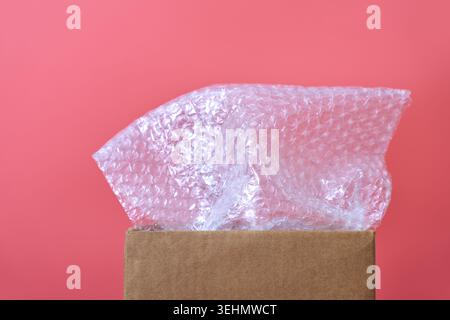 Transparente Luftpolsterpackung aus Kunststoff ragt vor einem rosafarbenen Hintergrund aus einem offenen Karton hervor und symbolisiert Verpackung, Versandschutz, Stauraum Stockfoto
