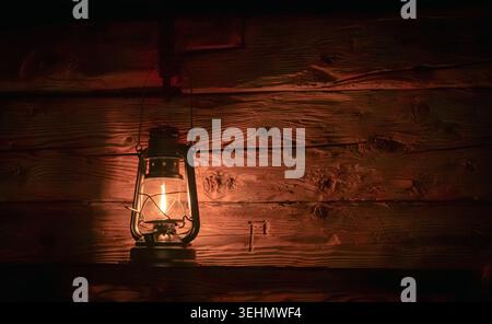 Eine Vintage-Laterne strahlt ein warmes, angenehmes Leuchten an einer rustikalen Holzwand aus und weckt ein Gefühl von Nostalgie und Einfachheit bei schlechten Lichtverhältnissen, ide Stockfoto
