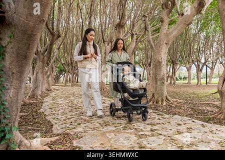 Eine Familie macht einen gemütlichen Spaziergang durch den Park und schiebt ein Baby im Kinderwagen auf einem baumgesäumten Weg. Die ruhige Atmosphäre ist perfekt zum Verbinden und r Stockfoto