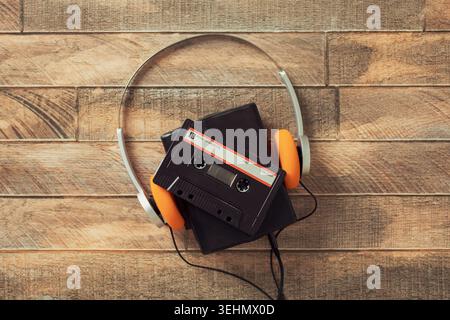 Draufsicht eines klassischen walkman ® Kassettenspielers mit orangefarbenen Kopfhörern und Klebeband auf rustikalem Holz, das an eine Retro-Ästhetik und Analog der alten Schule erinnert Stockfoto