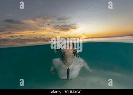Ozeanfoto auf zwei Ebenen von einem Taucher, der über einem Thila-Riff gleitet, halb unter Wasser und halb Himmel, mit warmem Sonnenuntergang, ruhigem Meer und tropischem adve Stockfoto