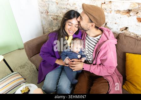 Warmes Lifestyle-Porträt einer glücklichen Familie mit einer neuen Mutter und einem neuen Vater, die ihr neugeborenes Baby auf einem gemütlichen Sofa zu Hause kuscheln und süße Momente der Liebe teilen, bo Stockfoto