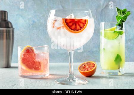Erfrischende Sommercocktails mit Gin Tonic und Mojito mit frischen Zitrusfrüchten. Ein Seitenblick auf lebendige Getränke vor einem kühlen blauen Hintergrund Stockfoto
