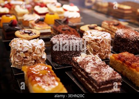 Nahaufnahme von verschiedenen Gebäckstücken und Mini-Kuchen in einer Bäckerei Vitrine mit Schokoladenstreuseln, Mandelscheiben, geschichteten Scheiben und Fruchtglasur u Stockfoto
